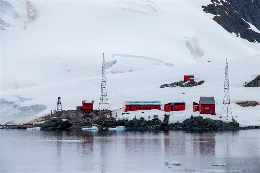 Red research station buildings beside the sea in a snowy Antarctic landscape