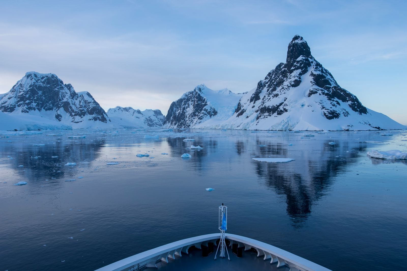 Ship&rsquo;s bow heading toward sharp snowy peaks reflected in still Antarctic water, the route south on Antarctic Circle cruises